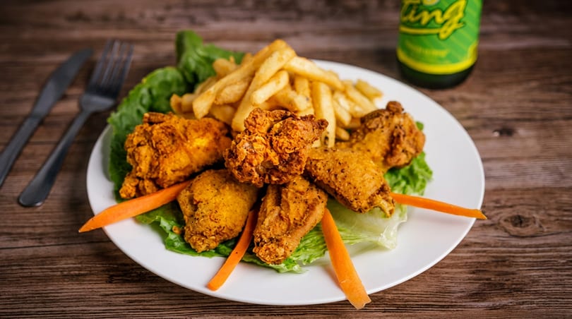 Crispy fried chicken wings and french fries on a white plate with lettuce and carrot sticks.